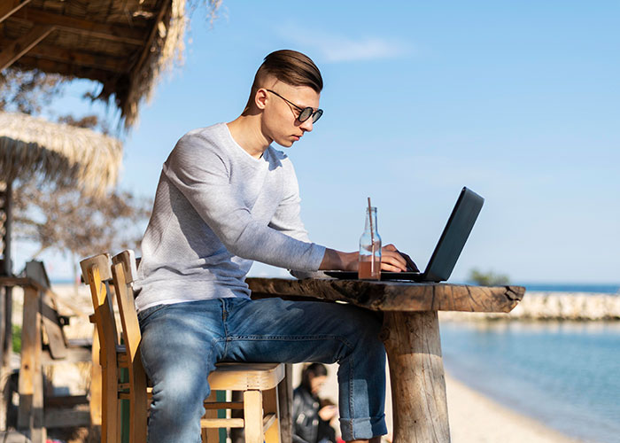 Person working on a laptop at a beachside café, looking focused and thoughtful.