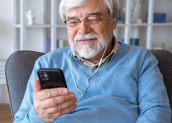 Elderly man with headphones smiling at phone, potentially involved in a deepfake scam. Elderly man with headphones smiling at phone, potentially involved in a deepfake scam.