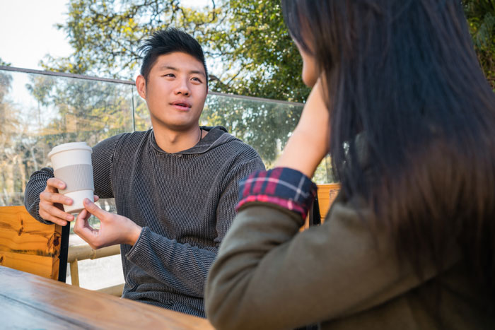 A man and woman in conversation outdoors, with the man holding a coffee cup, discussing Japanese culture. A man and woman in conversation outdoors, with the man holding a coffee cup, discussing Japanese culture.