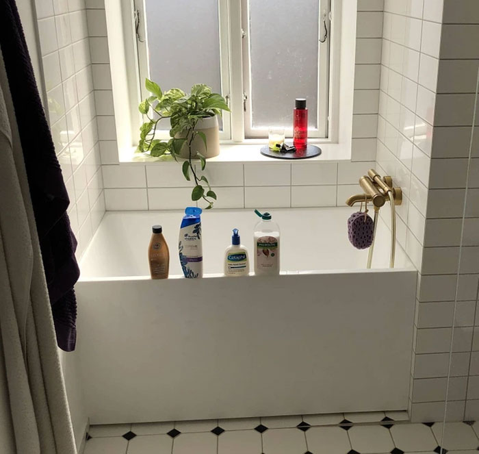 Bathtub with various toiletries and a plant on the windowsill.