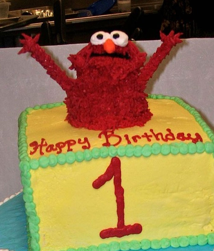 Cake with Elmo figure raising arms, referencing Elmo fire meme. Text reads "Happy Birthday" and a large "1".