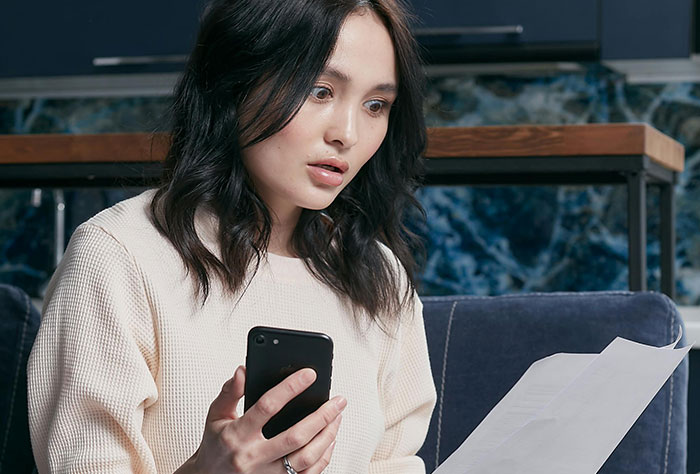 Woman holding a phone, surprised by a document, highlighting a house ownership issue.