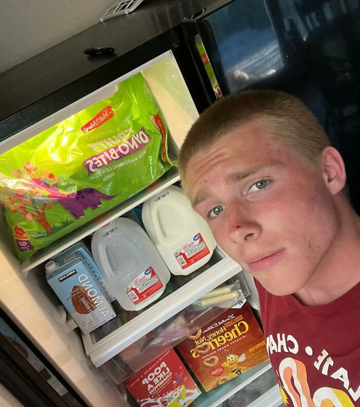Person posing with a chaotic fridge filled with cereal boxes and milk jugs. Ideal example of 'dude fridges'.