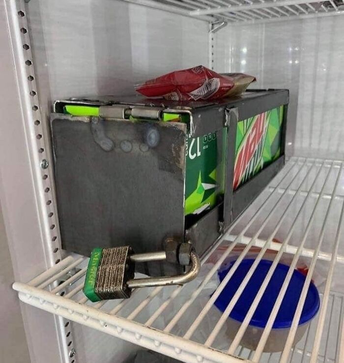 Chaotic fridge with locked Mountain Dew box and snacks on top shelf.