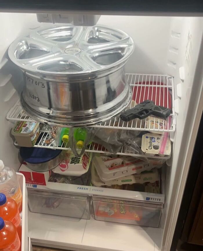A fridge filled with random items including a car wheel and a toy gun, showcasing a typical 'dude fridge' chaos.