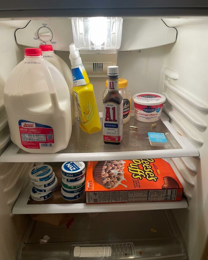 Inside view of a dude fridge with milk, condiments, cottage cheese, and Reese's Puffs cereal.
