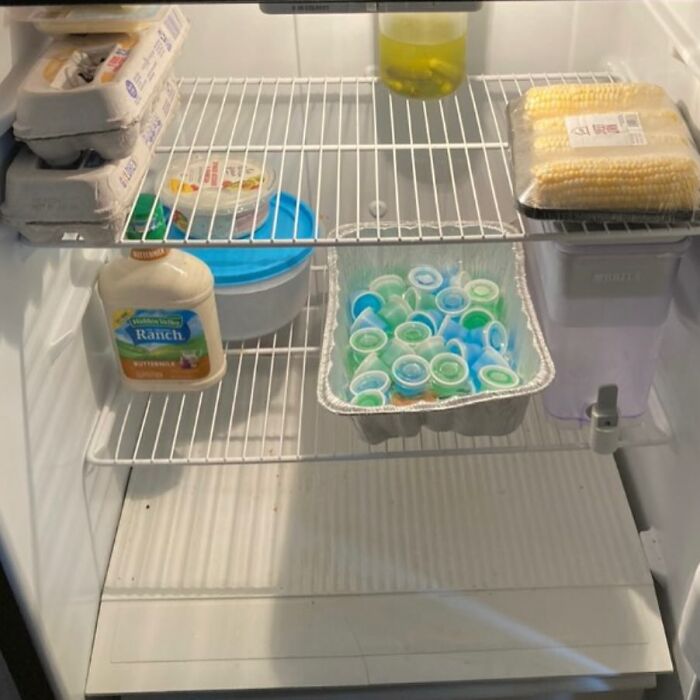 Chaotic dude fridge with eggs, ranch dressing, corn, Jell-O shots, and a Brita water filter.