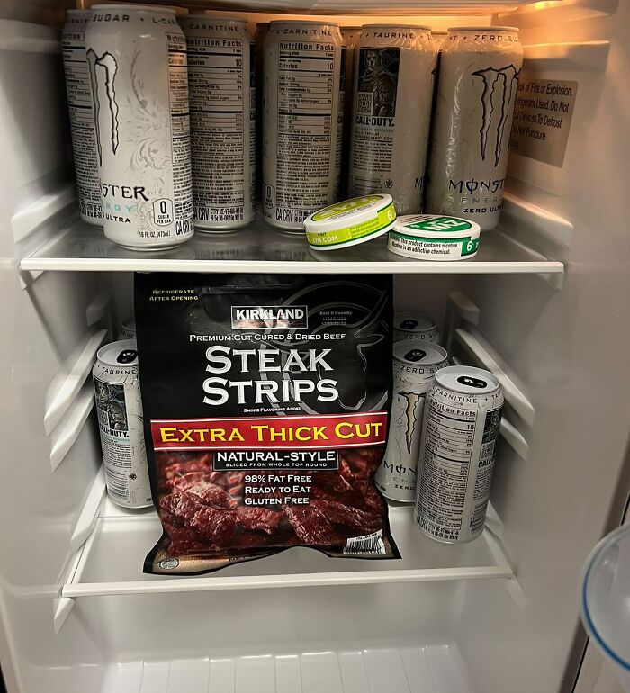 Dude fridge with energy drinks, steak strips, and dip cans neatly arranged on shelves.