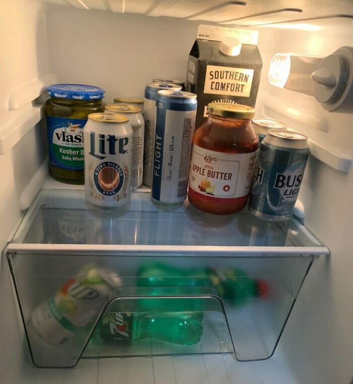 Open fridge with various drinks, pickles, apple butter, and alcohol; a typical example of a chaotic dude fridge.