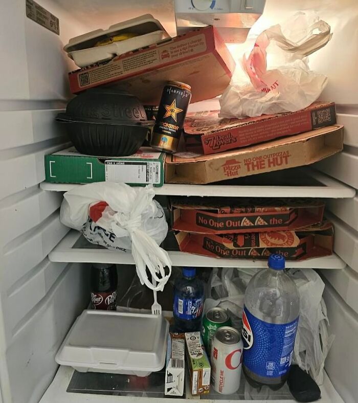 Chaotic dude fridge packed with pizza boxes, takeout containers, and assorted drinks.