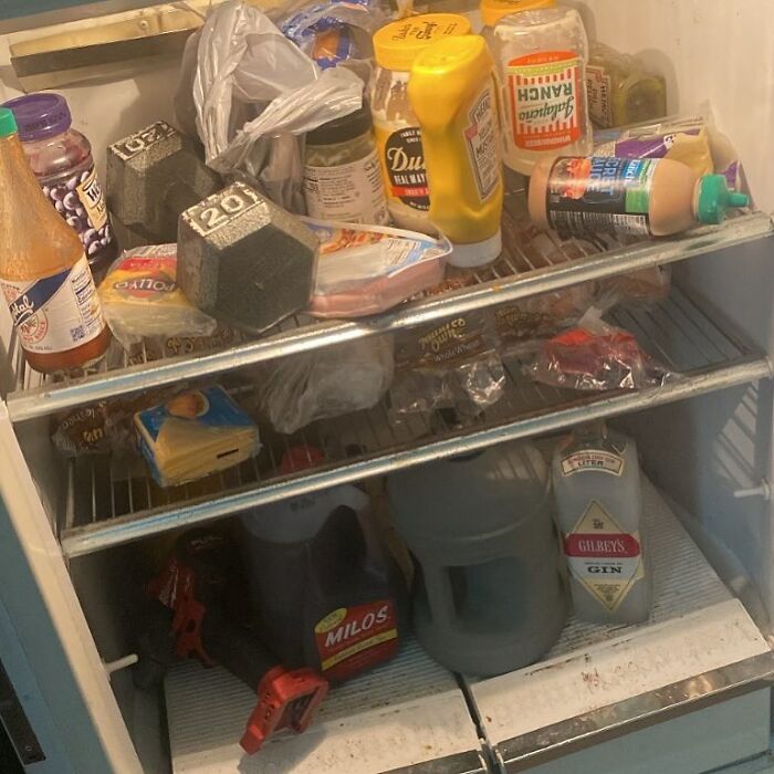 Chaotic dude fridge filled with condiments, drinks, and a dumbbell.