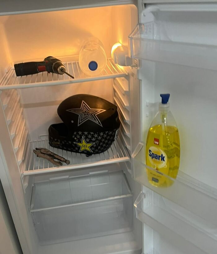 Open fridge with random items like a helmet, pliers, and dish soap, capturing the chaotic essence of dude fridges.