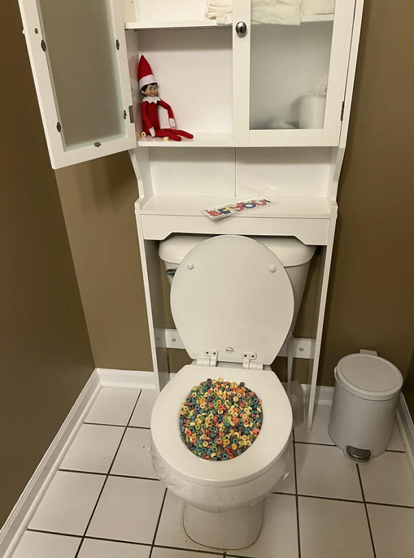 Elf On The Shelf sitting above a toilet filled with colorful cereal for a funny Elf On The Shelf idea in the bathroom.