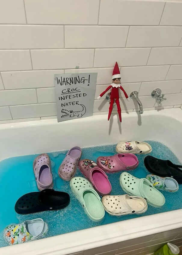 Elf On The Shelf hanging above bathtub filled with Crocs floating in blue water labeled croc infested water warning.