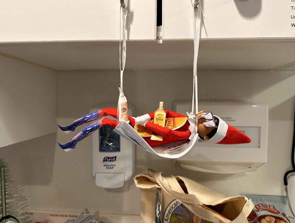 Elf On The Shelf lounging in a face mask hammock holding mini bottles, creating a mischievous holiday scene.