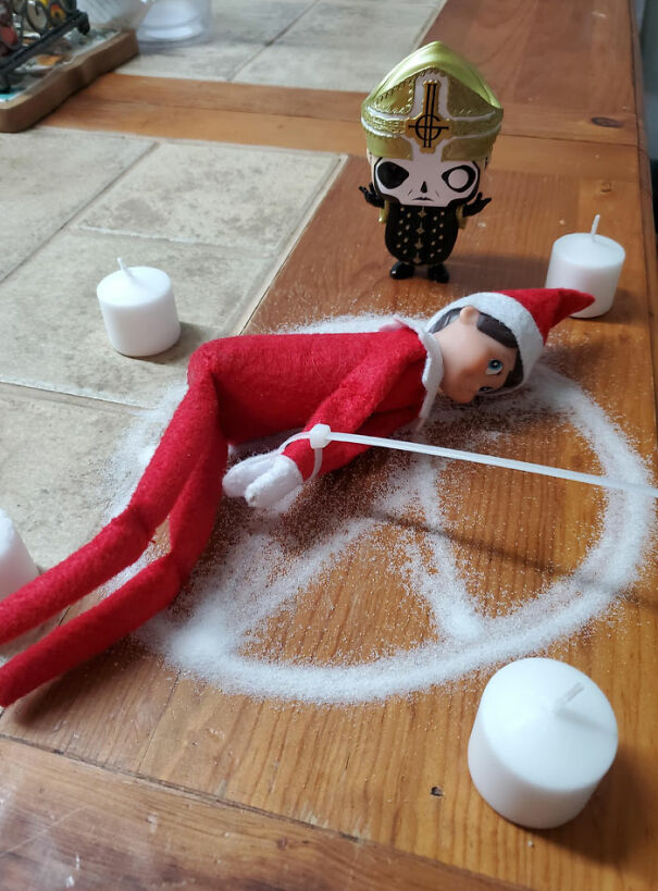 Elf On The Shelf in a salt circle with candles, tied up, next to a small figure in a spooky mischievous setup.
