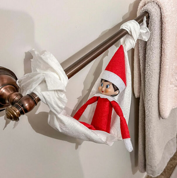 Elf On The Shelf idea with elf sitting in a toilet paper hammock hanging on a bathroom towel bar.