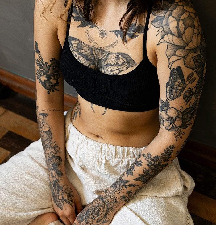 Young person with modern tattoos, showcasing floral and animal designs on arms and chest, illustrating 2024 tattoo trends.