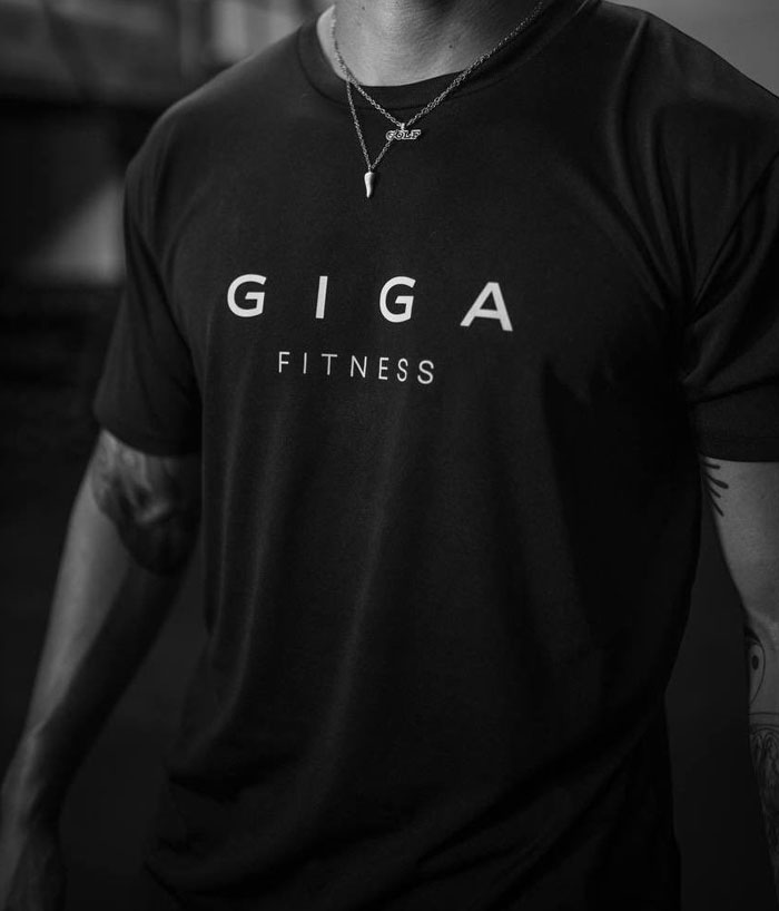 Grayscale image of person in "GIGA FITNESS" T-shirt, representing the Giga Chad meme and extreme masculinity concept.