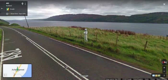 Person in a white suit standing beside a Scottish road, captured on Google Street View.