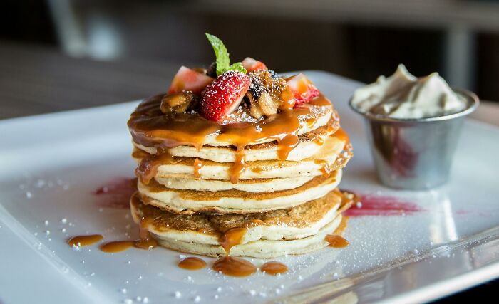 Stack of pancakes with caramel sauce and strawberries, evoking smell happiness, served with whipped cream on a white plate.