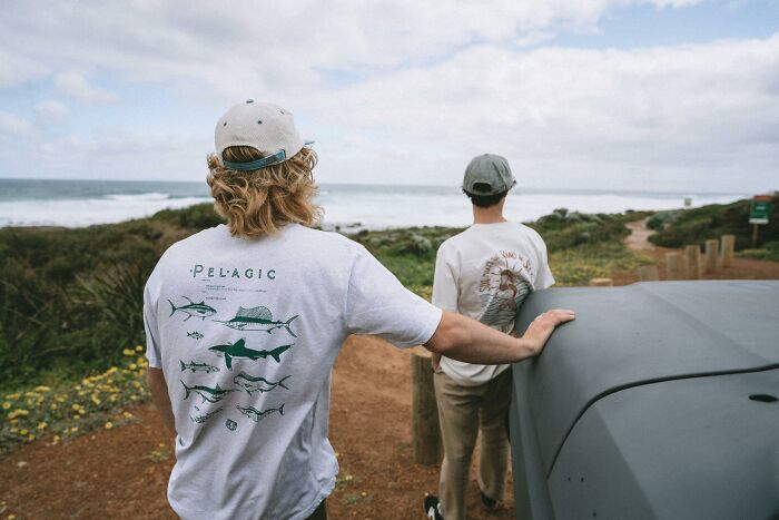 Two people enjoy a coastal view, wearing casual shirts and hats, embodying a sense of happiness outdoors.