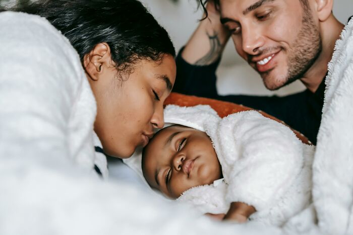 Family cuddling with their baby, wrapped in white blankets, enjoying a moment of peace and happiness.