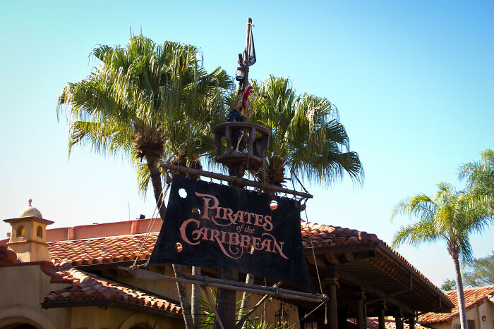 Pirates of the Caribbean sign in front of palm trees under a clear blue sky, capturing theme park joy and excitement.