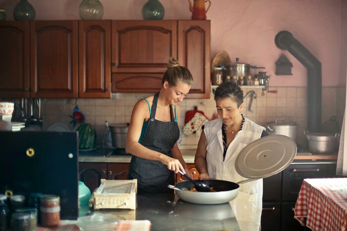 Two women cooking together in a cozy kitchen, sharing a moment of smell happiness over a simmering pot.