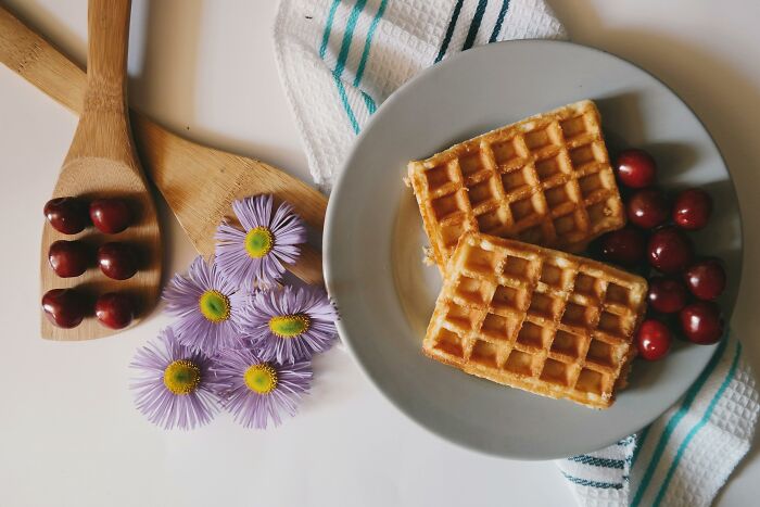 Plate of waffles with cherries, surrounded by flowers and kitchen towels, evoking a sense of smell-happiness.