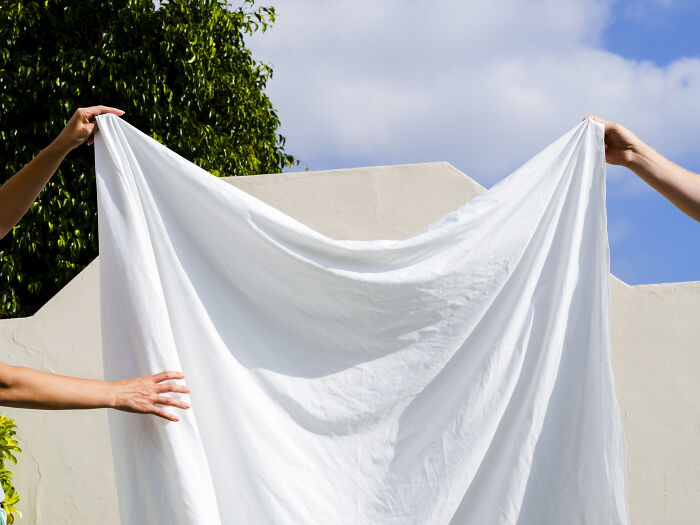 Two people holding a fresh white sheet outdoors under a blue sky, symbolizing smell-happiness from Reddit discussions.