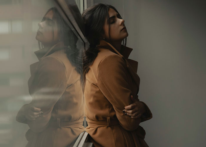 Woman in a tan coat leans against a window, reflecting on a friendship revelation.