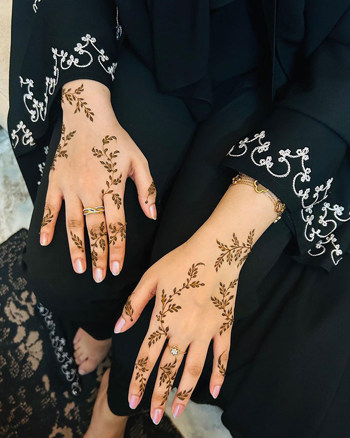 Hands adorned with intricate henna tattoo designs, showcasing stunning patterns on a black outfit.