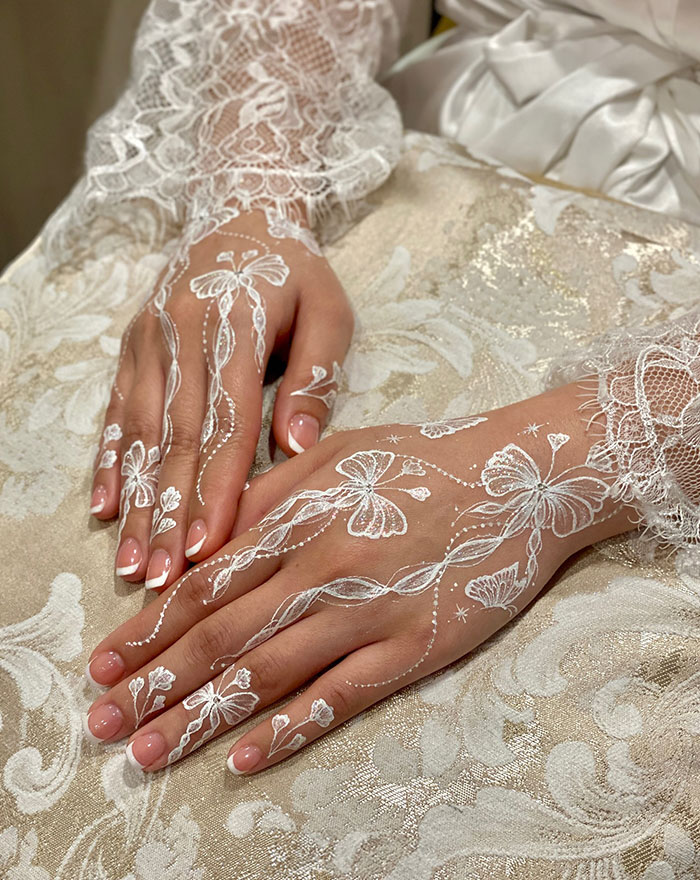White henna tattoo design on hands, featuring intricate floral patterns and butterflies.