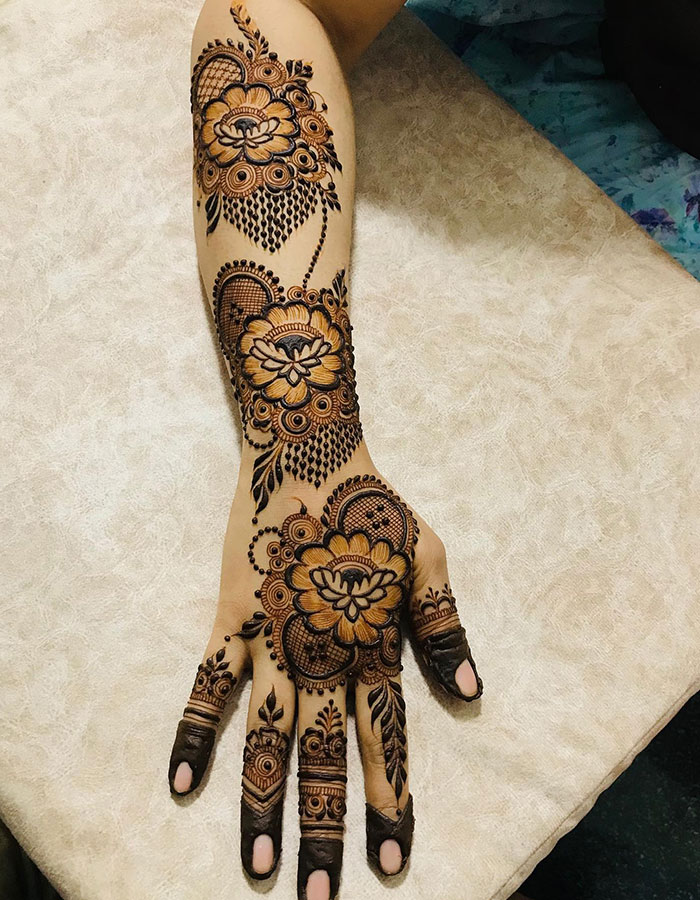 Intricate henna tattoo design covering forearm and hand, showcasing floral patterns and detailed artistry.