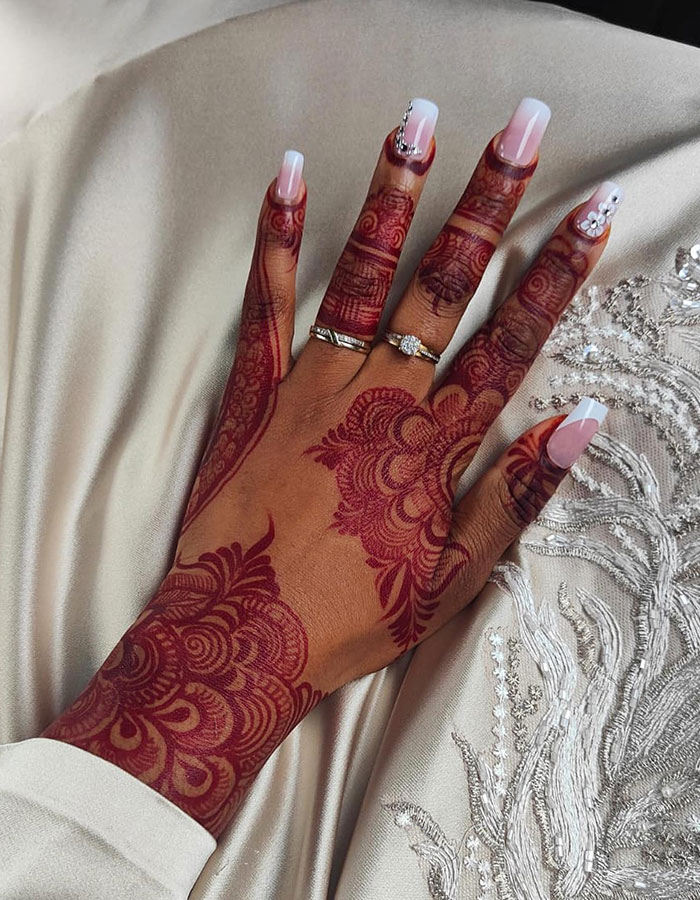 Intricate henna tattoo design on hand with rings, featuring floral patterns and elegant nail art.