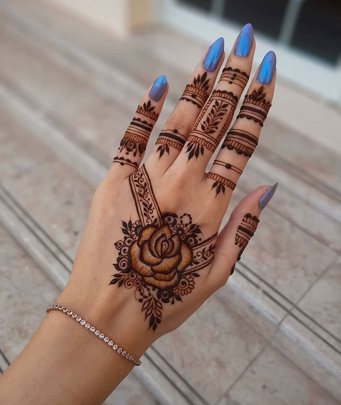 Hand adorned with an intricate henna tattoo design featuring a floral pattern extending over fingers.