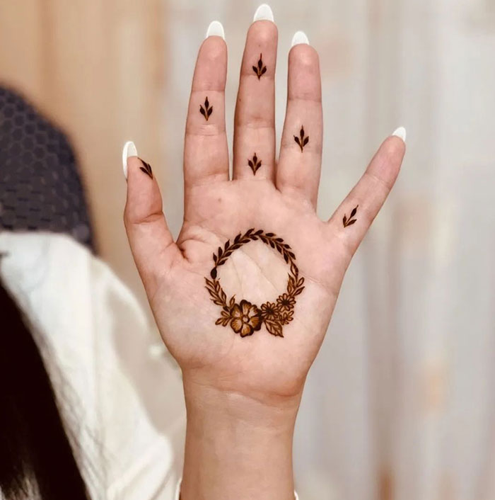 Hand with intricate henna tattoo design, featuring floral and leaf patterns on the palm and fingers.