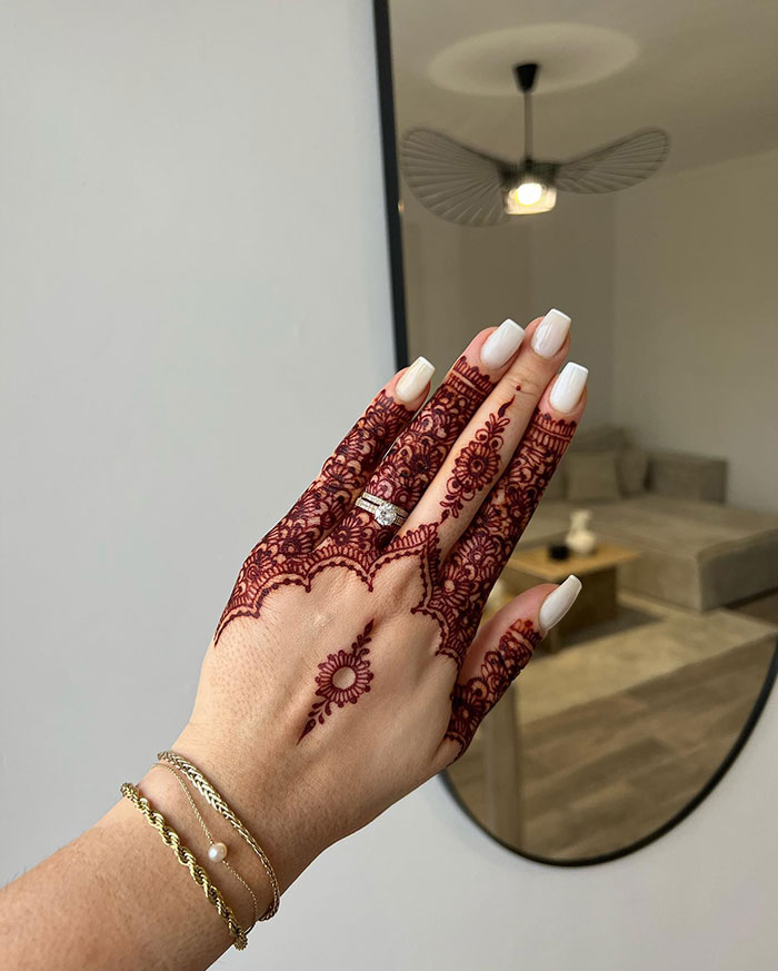 Hand adorned with intricate henna tattoo design, showcasing elegance and artistry in a modern living room setting.
