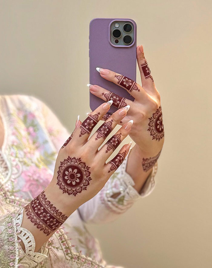 Hands with intricate henna tattoo designs holding a purple phone.