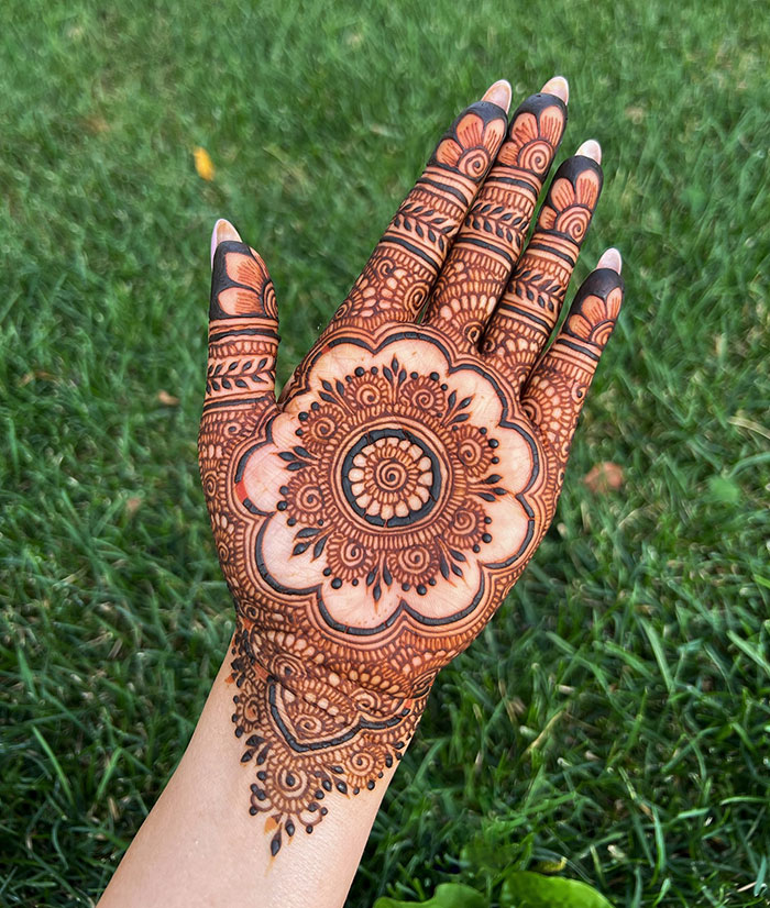 Intricate henna tattoo design on a hand, showcasing stunning patterns on a green grassy background.