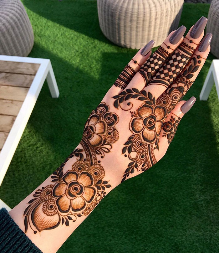 Intricate floral henna tattoo on a woman's hand, showcasing stunning design ideas in a garden setting.