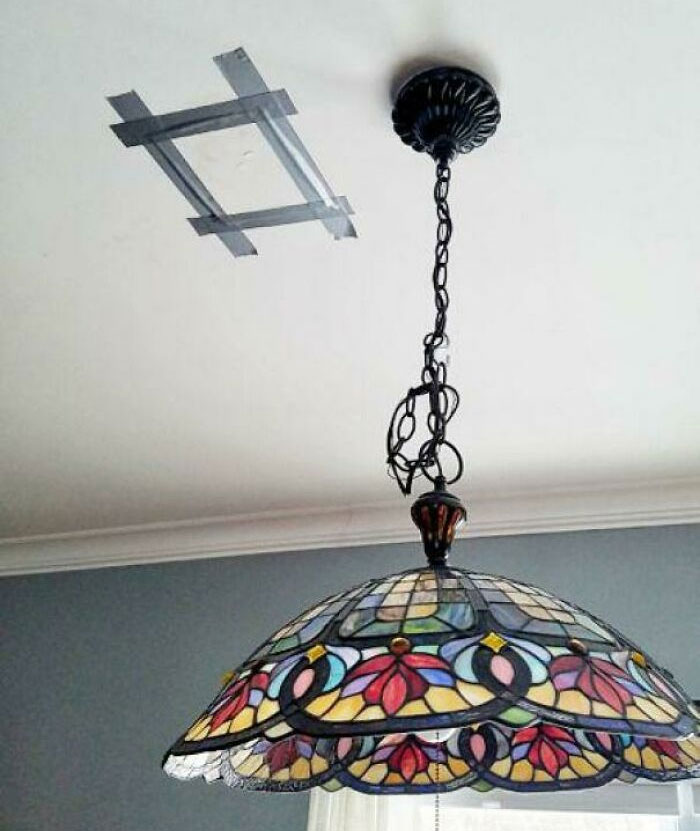 Stained glass lamp humorously misaligned with ceiling fixture, creating a hilarious in-laws DIY moment.