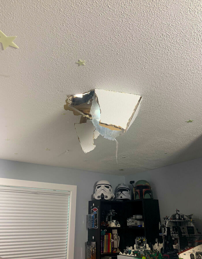 Ceiling with large hole, result of home improvement fail, above a shelf of collectibles in a room.