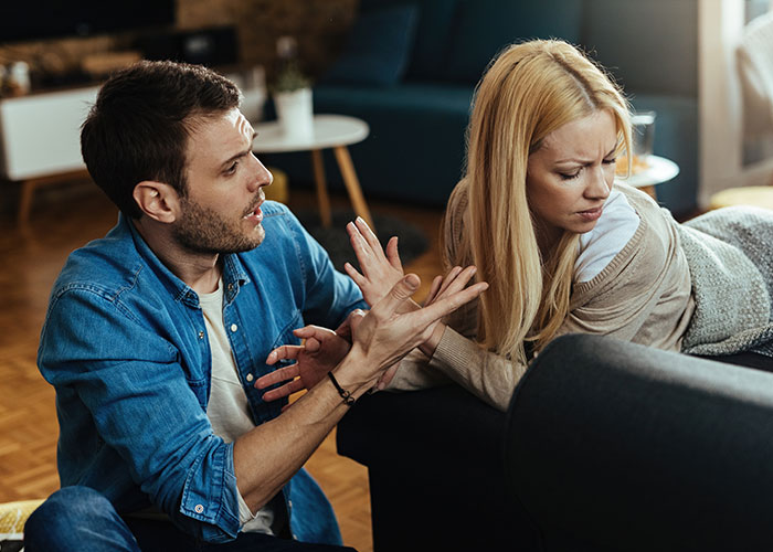 Husband and wife having a serious discussion on the couch, highlighting tension and emotion in the room.