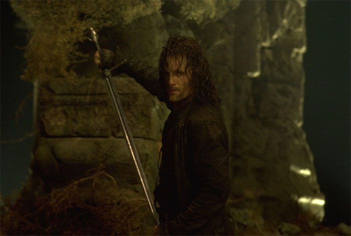 Actor in a dark setting, holding a sword, embodying a role with remarkable precision and intensity.