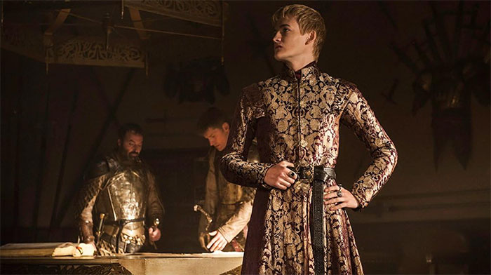 Actor in ornate medieval costume, standing confidently in a dimly lit room, embodying a role flawlessly.