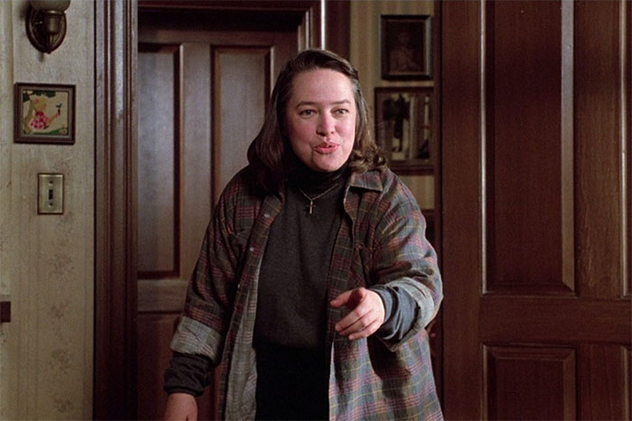 Actor flawlessly portraying a character with intensity in a home setting, wearing a plaid shirt over a dark turtleneck.