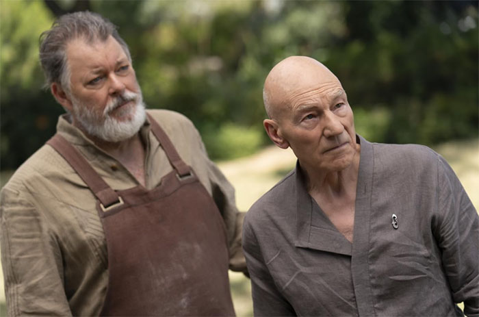 Two actors in character, one wearing an apron and the other in casual attire, embodying flawless roles outdoors.