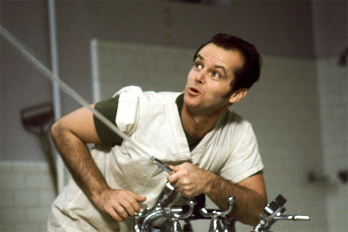 Actor in iconic role, wearing a white shirt, mimicking a quirky expression in a classic film scene.